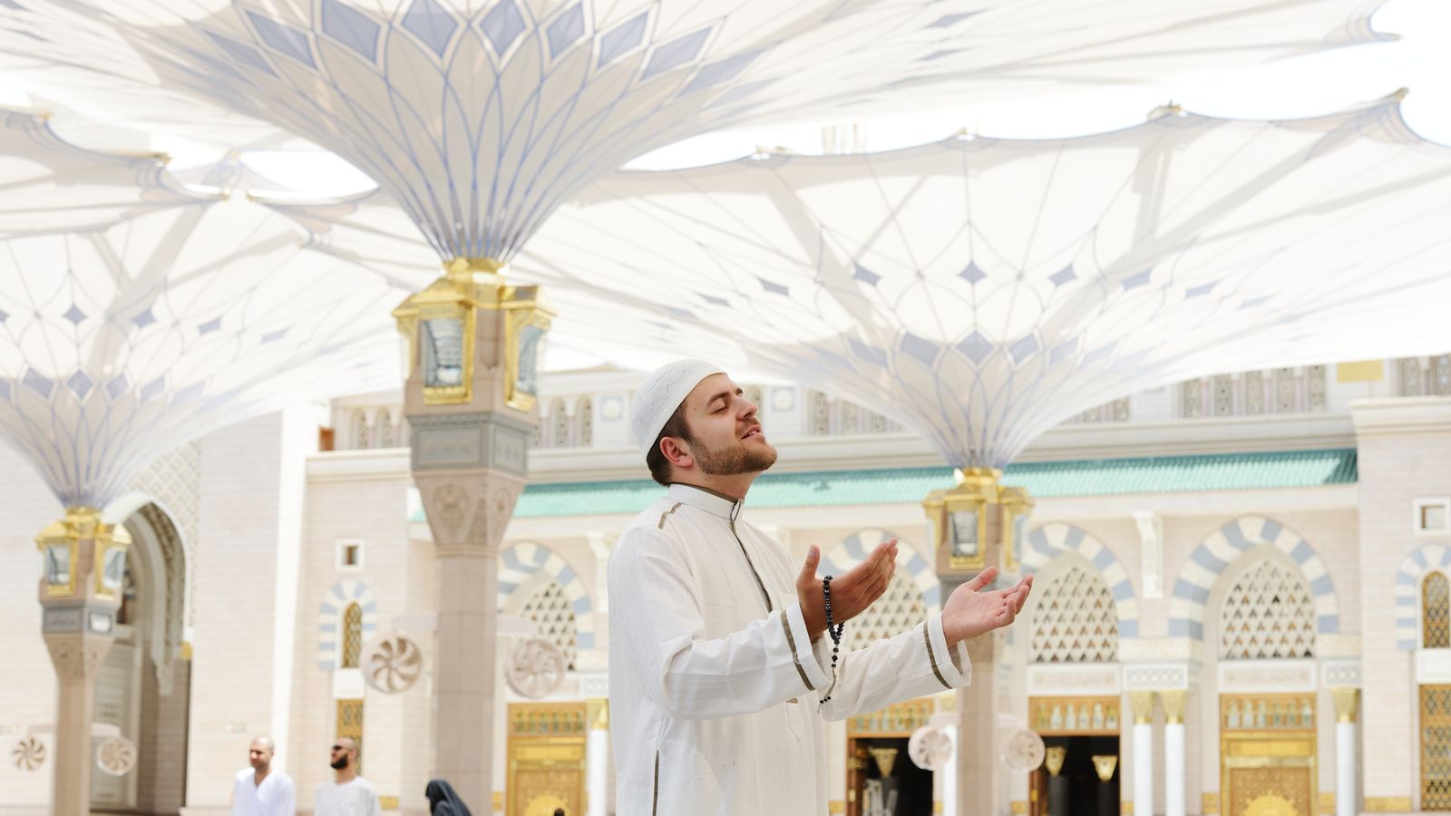 Muslim man praying at Masjid an-Nabawi under white umbrellas during Umrah journey, ideal for Umrah Packages 2025.